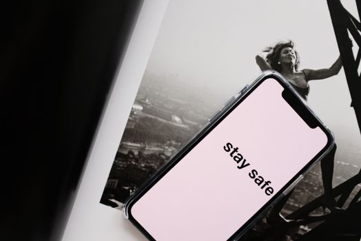 From above of cellphone with pale pink screen and STAY SAFE inscription put on open magazine with image of cheerful female climbing metal tower