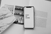 平躺的单色智能手机上显示着“呆在家里”的信息，旁边放着一本打开的书，以促进家庭学习