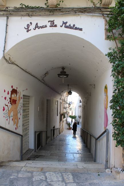 Fotomural Un pintoresco arco en Italia con murales divertidos y un camino empedrado.