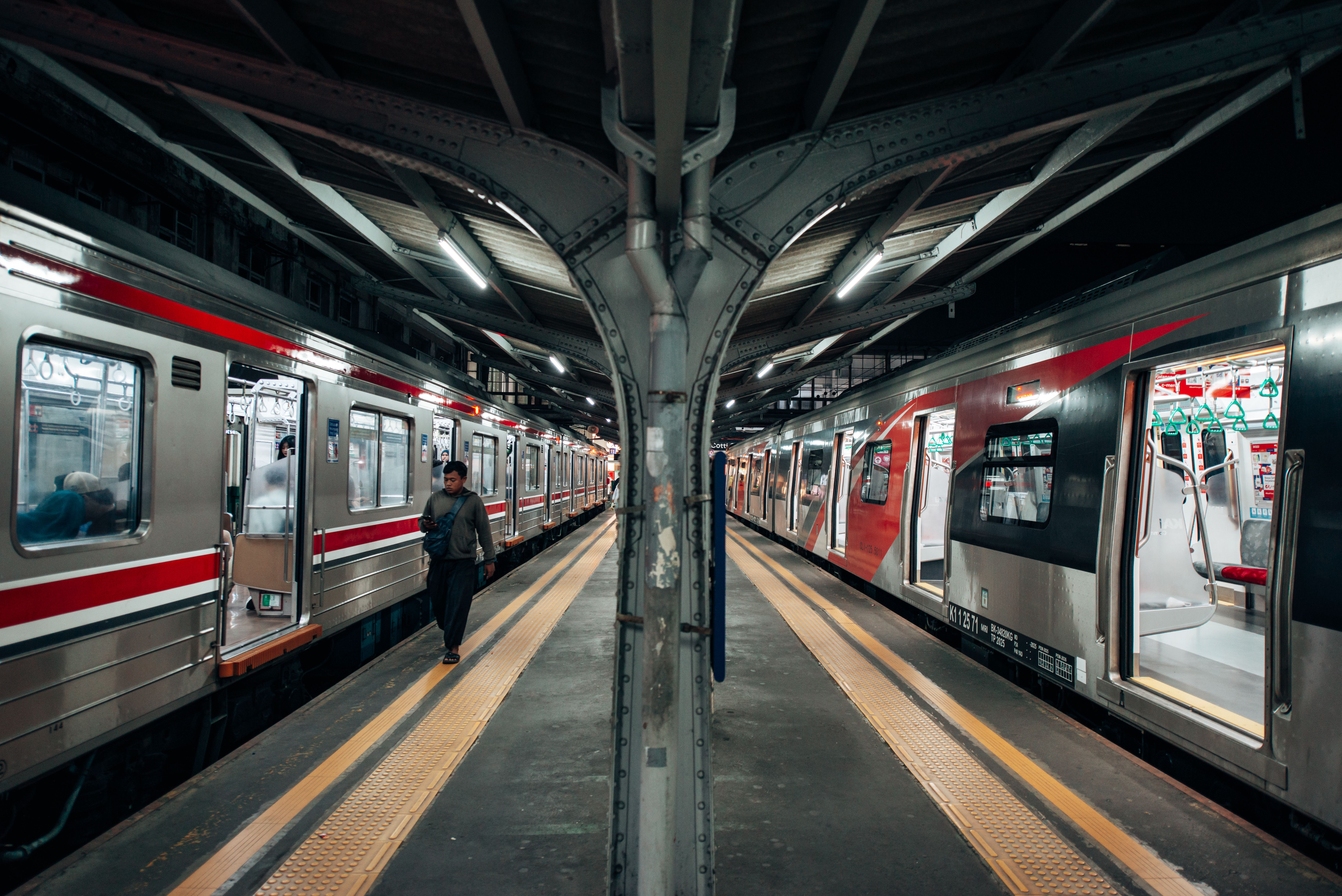 A bustling urban train station with trains on both sides and a few passengers on the platform.