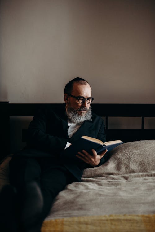 수염 난된 남자가 침대에서 책을 읽고