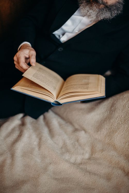 Free Senior man in black suit reading a book while lying in bed. Stock Photo