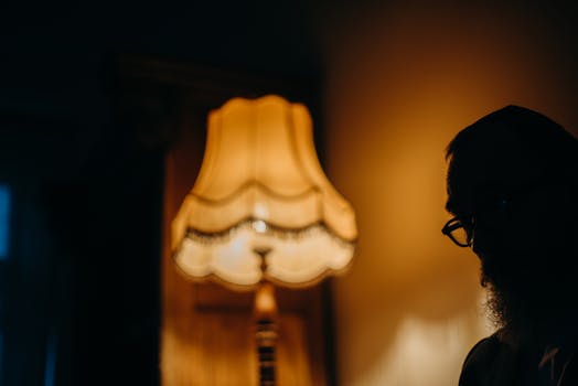 Silhouette of a bearded man beside a vintage lamp casting a warm glow.