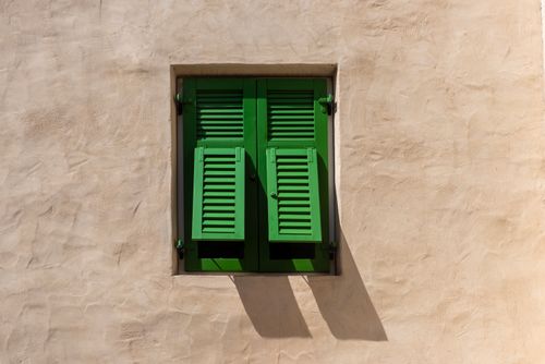 Free Vivid green shutters contrast beautifully against a textured beige plaster wall, casting elegant shadows. Stock Photo