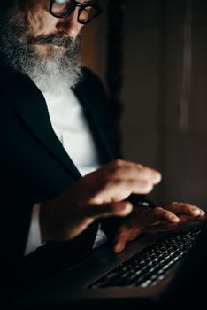 An adult man with a beard using a laptop indoors, engaged in remote work.