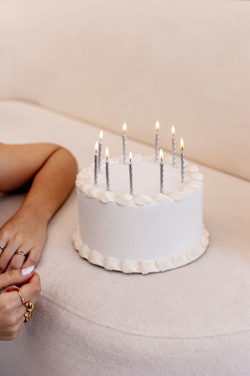 Free Minimalist white cake with lit candles beside a person's hands, celebrating a birthday. Stock Photo