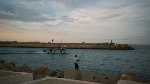Free A serene fishing scene at an Algerian harbor with a boat at sunset, reflecting tranquility and daily life. Stock Photo