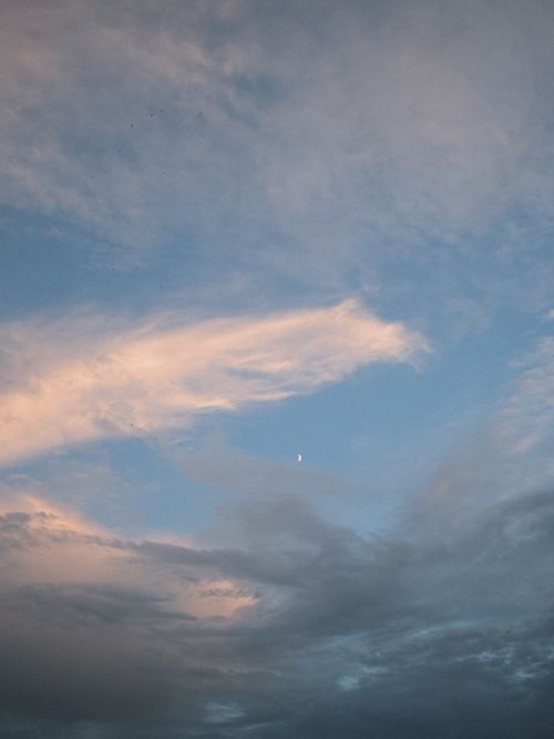 Free Calm evening sky with scattered clouds and a crescent moon, creating a peaceful ambiance. Stock Photo