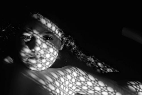 Free Artistic black and white portrait of a girl with intriguing light patterns on her face. Stock Photo
