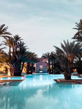 A serene evening view of a tropical resort pool surrounded by palm trees under a clear sky.