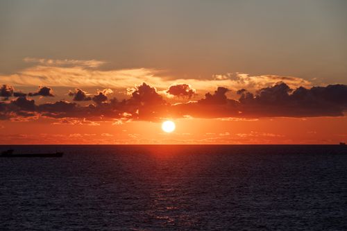 Free A breathtaking view of the sunset over the ocean with vibrant orange and red clouds. Stock Photo