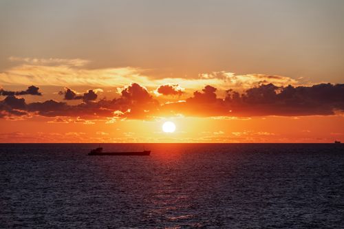 Free A breathtaking sunset over the ocean with a cargo ship silhouette and vibrant cloud colors. Stock Photo