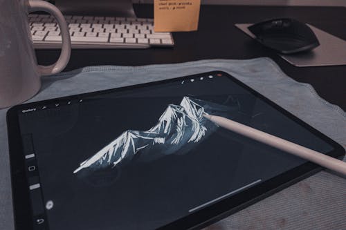 Modern electronic drawing tablet with mountain on display and stylus composing with keyboard and cup of coffee