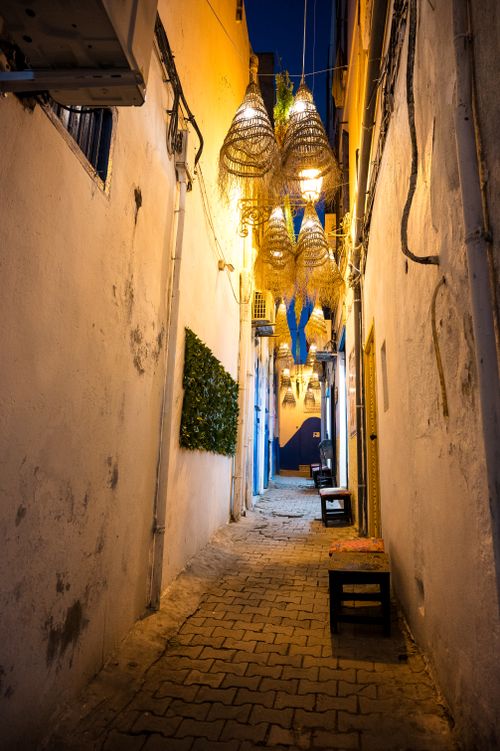 Free Serene night scene of a narrow alley in Tunis Medina, featuring traditional lamps and whitewashed walls. Stock Photo