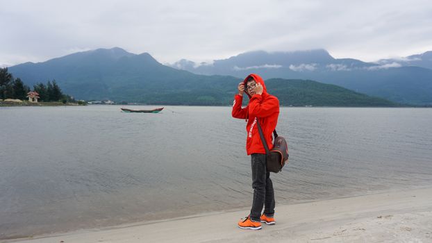 A person enjoys the serene beach landscape in Da Nang, Vietnam, wearing a bright red hoodie.