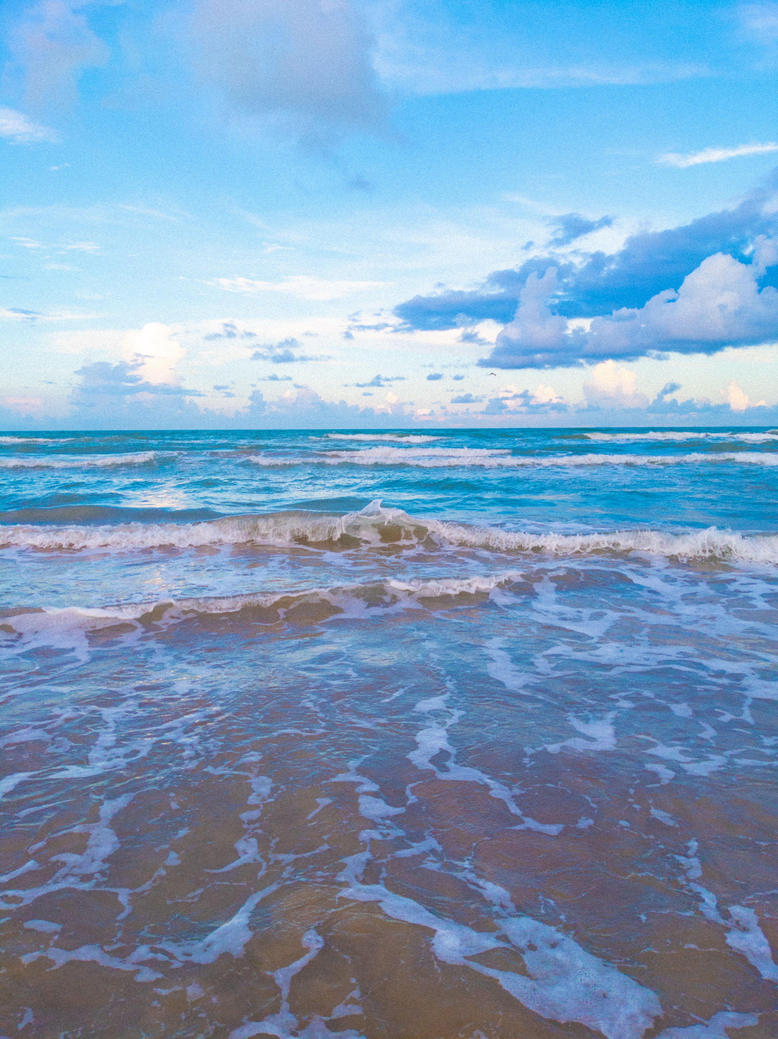 Calm ocean waves gently lap the sandy beach under a clear blue sky, creating a serene coastal scene.