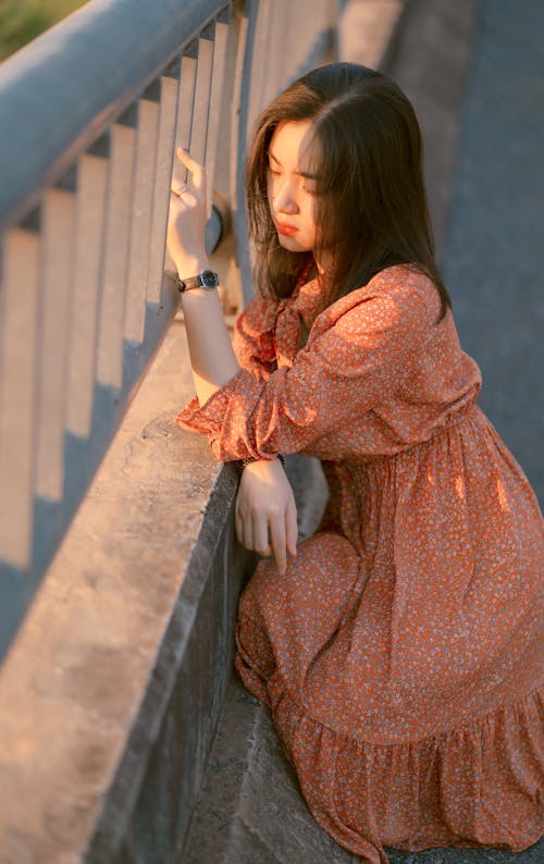 Free Woman in Brown Long Sleeve Dress Leaning On An Iron Railings Stock Photo