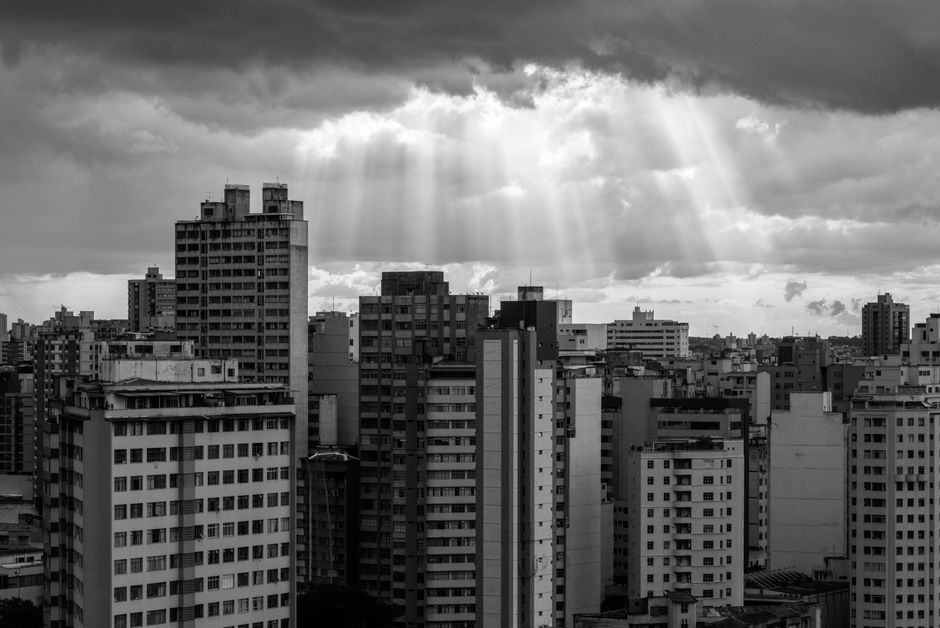 Black and white photo of Belo Horizonte skyline under dramatic sun rays breaking through clouds.