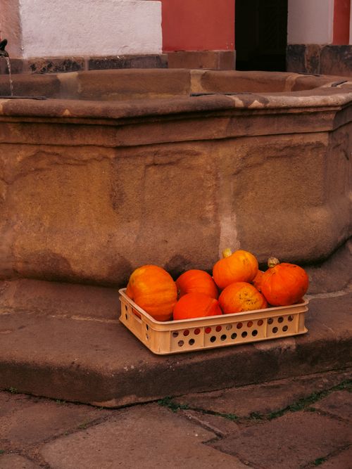 Free A wooden crate of orange pumpkins set by a rustic stone well in Czechia. Stock Photo