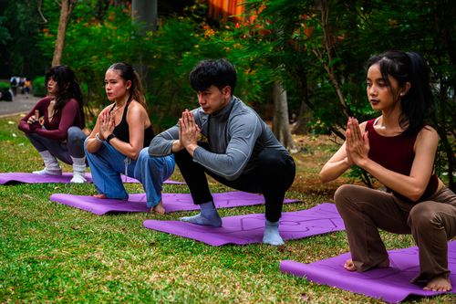 Free Four adults practicing yoga on purple mats in a Jakarta park, showcasing wellness and mindfulness. Stock Photo