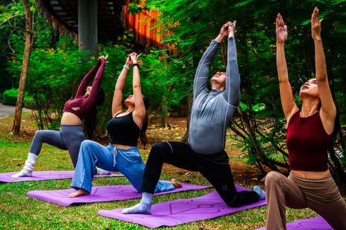 Free Four people practicing yoga outdoors in a lush Jakarta park, emphasizing health and mindfulness. Stock Photo