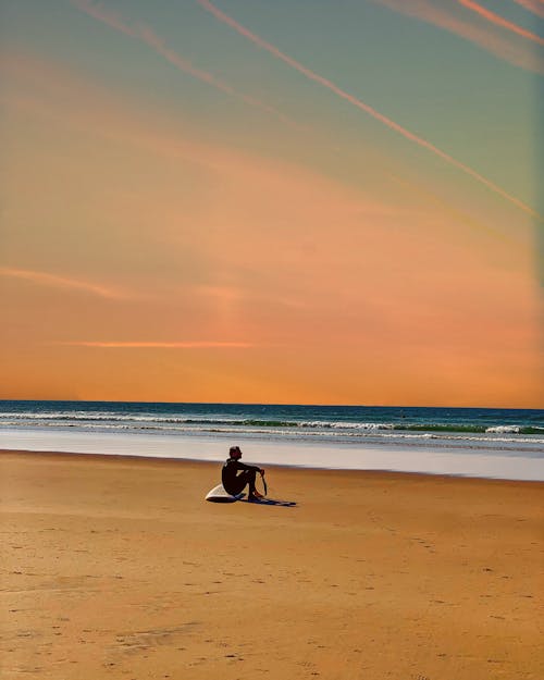 Man Sitting on Beach Shore During Sunset
