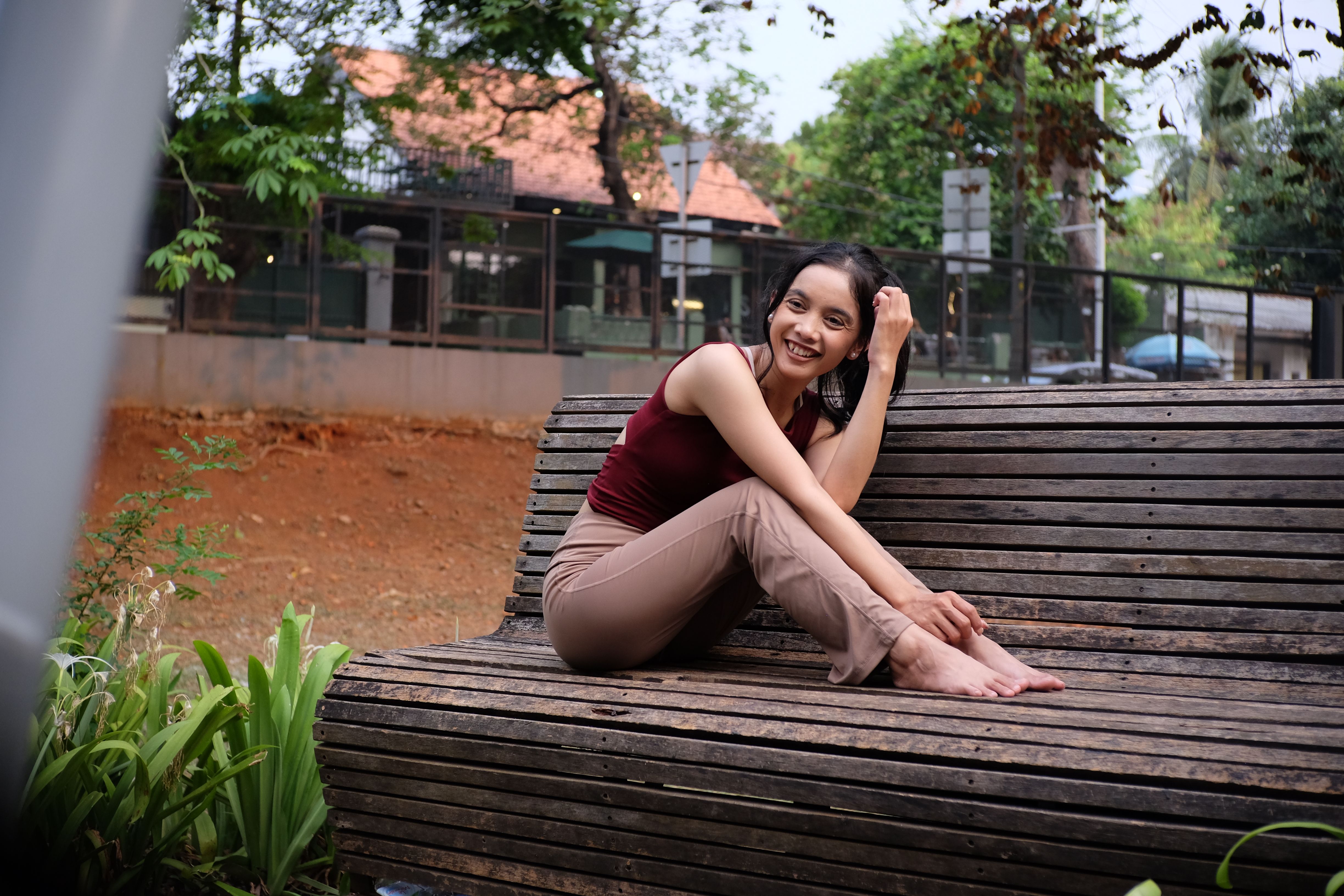 Woman smiling and relaxing on a wooden park bench outdoors