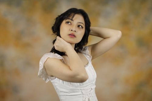 Free Charming portrait of a young woman in a white dress posing gracefully against a warm background. Stock Photo