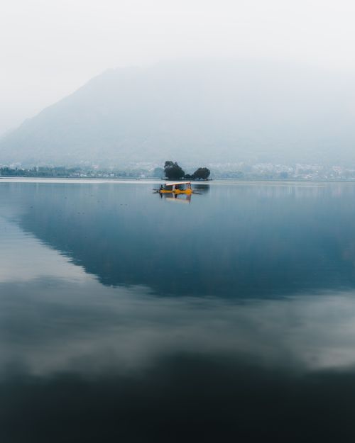 Free A serene view of a shikara boat on Dal Lake amidst misty mountains in Srinagar. Stock Photo