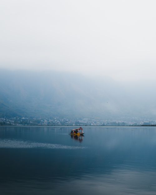 Free Peaceful scene of a shikara boat on Dal Lake with mountains in the background. Stock Photo