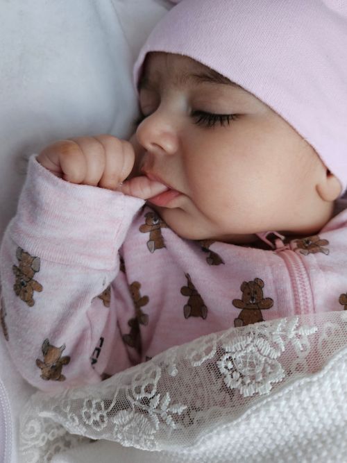 Free Adorable infant sleeping peacefully, thumb in mouth, wearing pink outfit and hat. Stock Photo