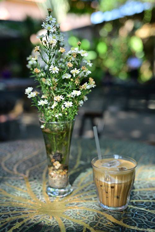 Free Glass vase with white flowers and iced coffee on an ornate outdoor table. Stock Photo