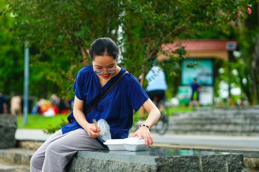 A woman sitting outdoors enjoying traditional Hue street food from a takeout container.