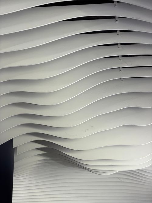 Free Elegant white wave-like ceiling panels creating a modern abstract design indoors. Stock Photo