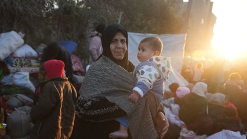 Free A mother embraces her child amidst a refugee camp, illuminated by a warm sunset glow. Stock Photo