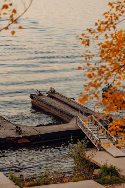 Free Peaceful lakeside dock surrounded by autumn leaves at sunset, creating a warm and serene atmosphere. Stock Photo