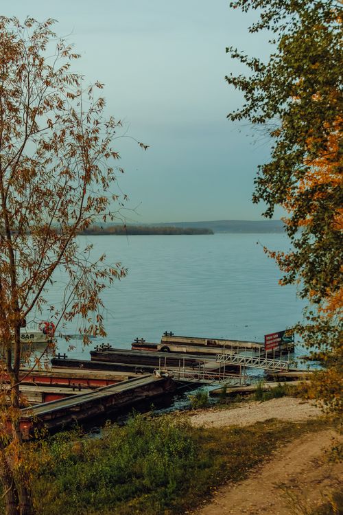 Free Scenic lakeside view with boats docked under autumn trees, offering a tranquil outdoor retreat. Stock Photo