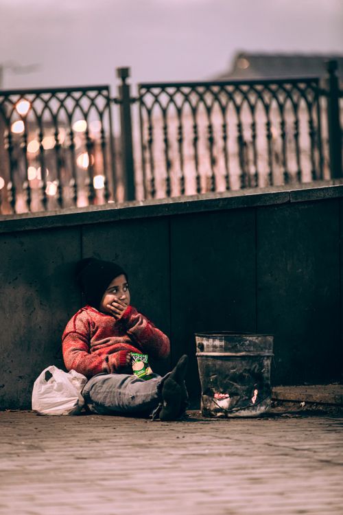 Free A young child sits on the street by a small fire in Istanbul, Türkiye, wearing a red sweater. Stock Photo