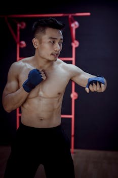 Muscular young naked Asian bodybuilder thoughtfully looking away while practice Muay Thai while training in gym