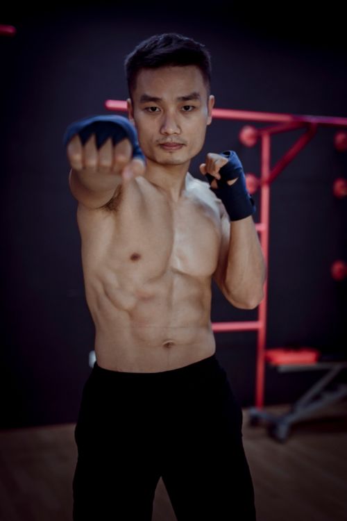 Free Serious young shirtless muscular male fighter in black pants and ace bandages confidently looking at camera while doing Thai boxing Stock Photo