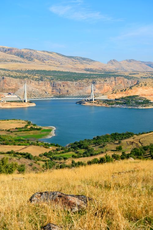 Free Aerial view of a stunning bridge over a river surrounded by hills under a clear blue sky. Stock Photo