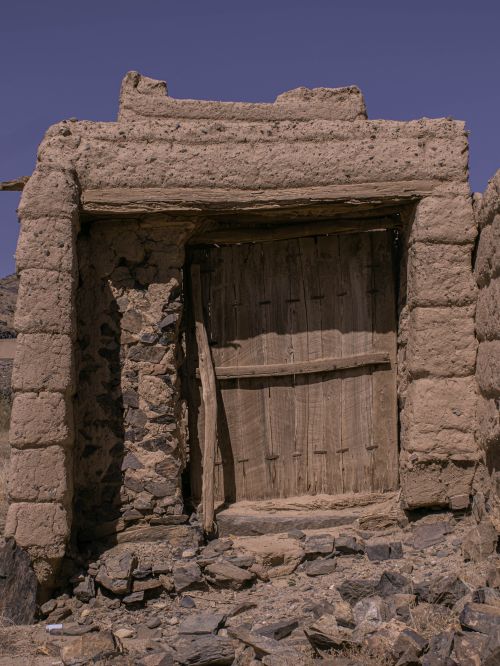 Free Weathered wooden door set in ancient stone structure under clear skies. Stock Photo