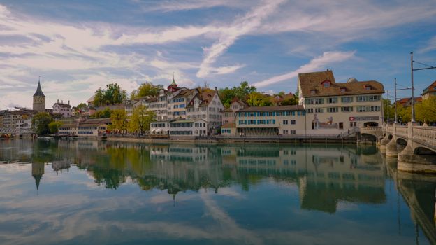 Picturesque view of historic buildings along Limmat river in Zurich, Switzerland reflecting in calm water.