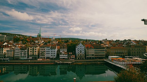Scenic view of Zurich's historical buildings reflecting over the serene Limmat River under a vibrant sky.