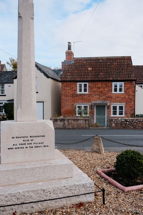 Free Village war memorial in front of historic brick house, serene setting. Stock Photo