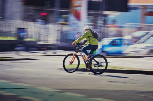 Free A cyclist wearing a green jacket riding swiftly on city streets, showcasing motion blur. Stock Photo