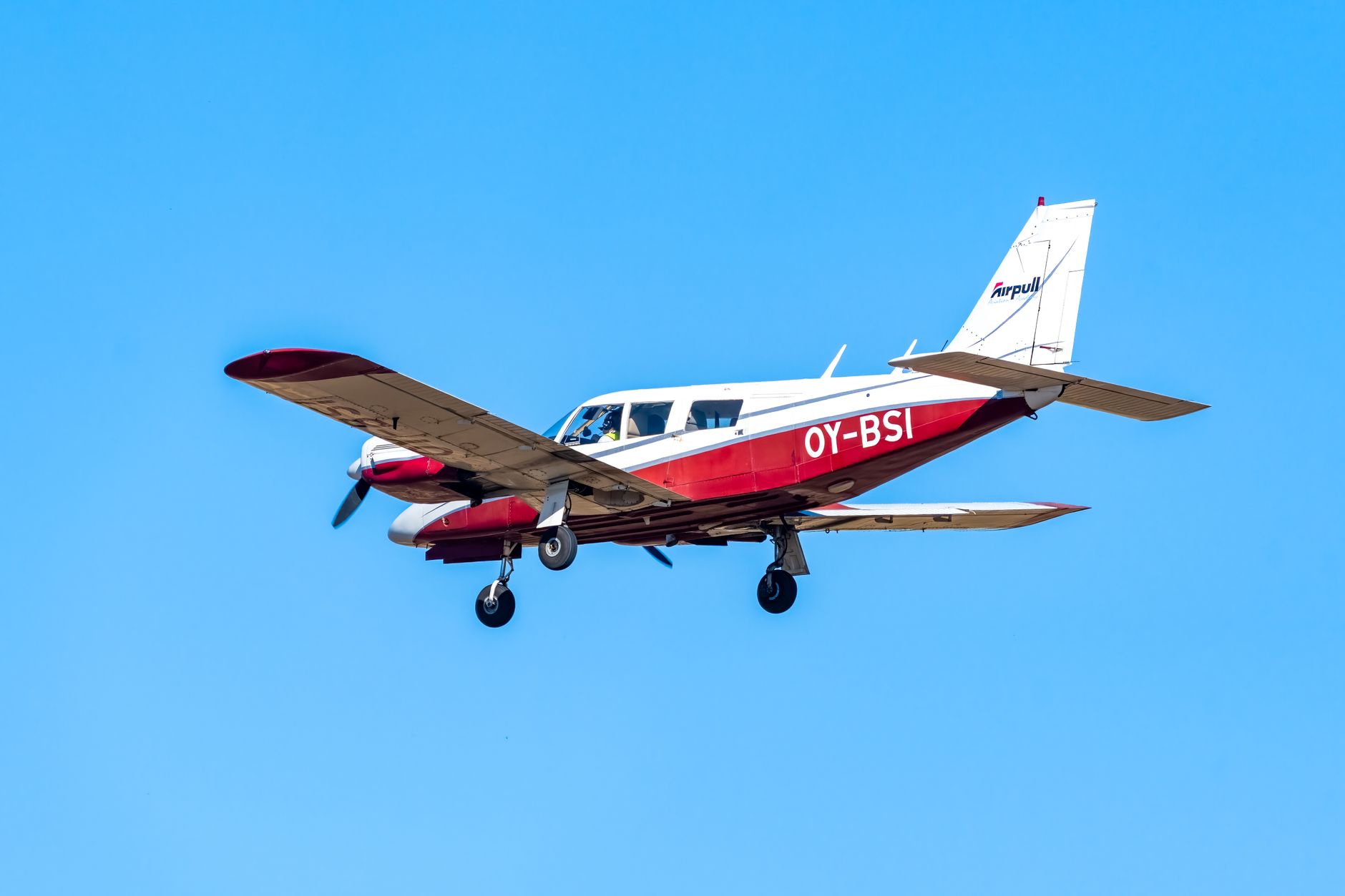Red and white small aircraft flying in a clear blue sky, showcasing aviation.