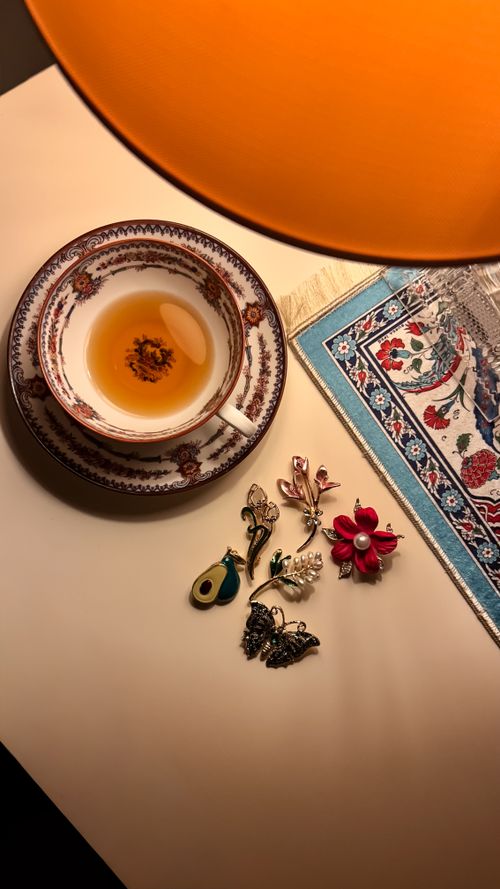 Free Elegant tea cup and saucer with floral brooches on a warm-lit table setting. Stock Photo