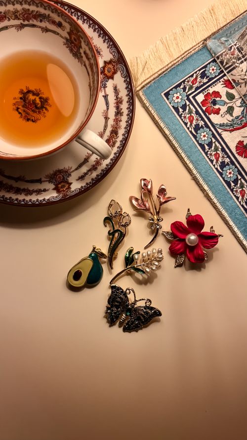 Free A close-up view of a cup of tea with intricate brooches on a table, showcasing elegance and style. Stock Photo