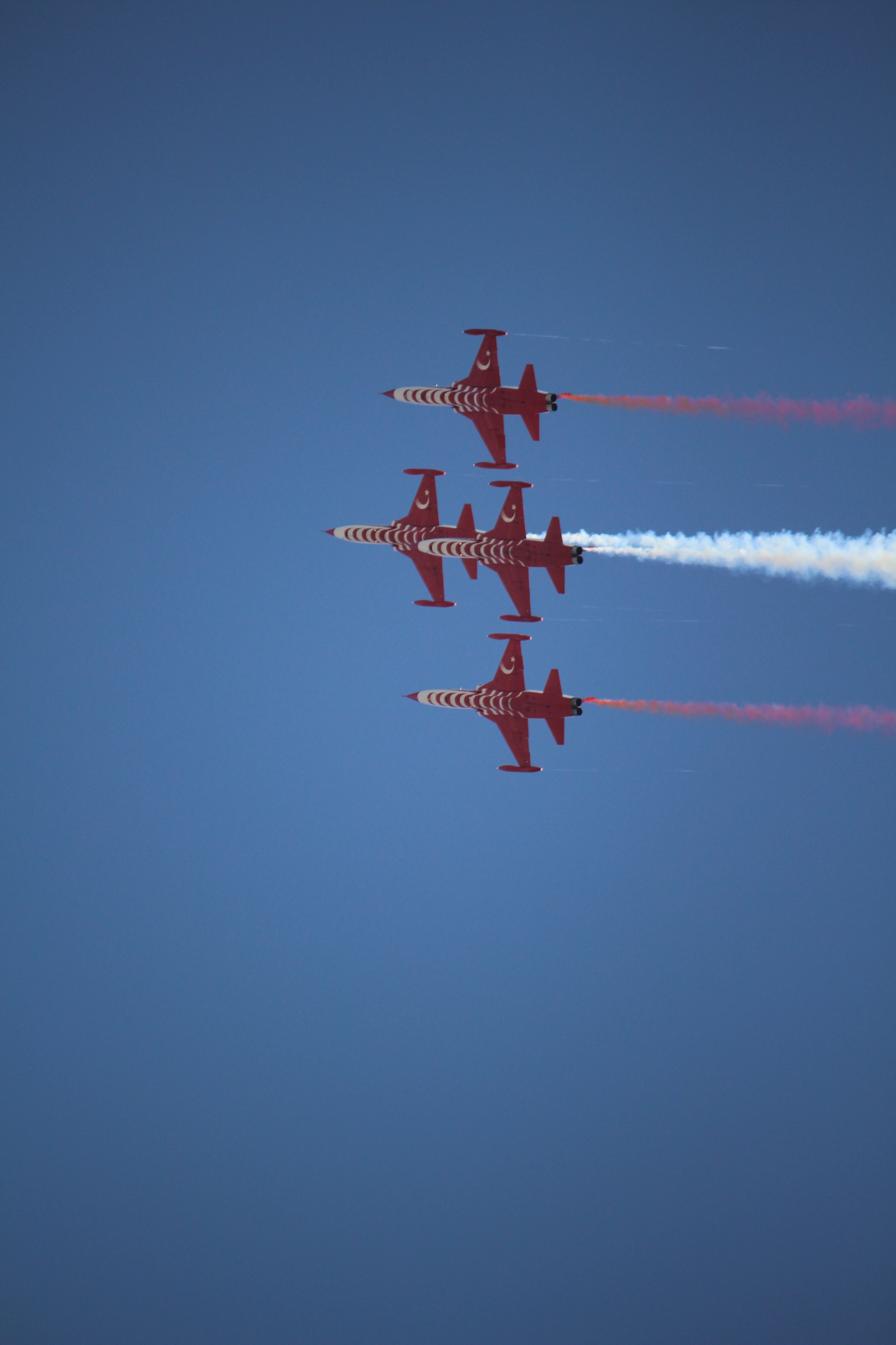 Fotomural Cuatro aviones rojos de un equipo acrobático realizando vuelos sincronizados bajo un cielo azul.